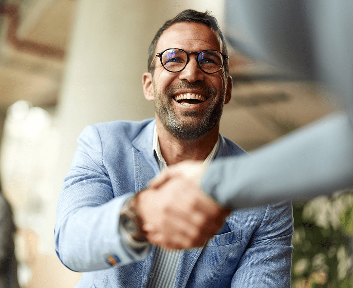 Lächelnder Geschäftsmann im blauen Sakko beim Händeschütteln als Symbol für erfolgreiche Zusammenarbeit