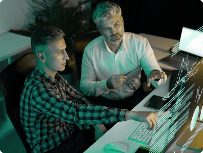 Zwei Fachkräfte arbeiten gemeinsam am Computer mit eingeblendeten Datenvisualisierungen zur Analyse und Entwicklung von IoT-Systemen