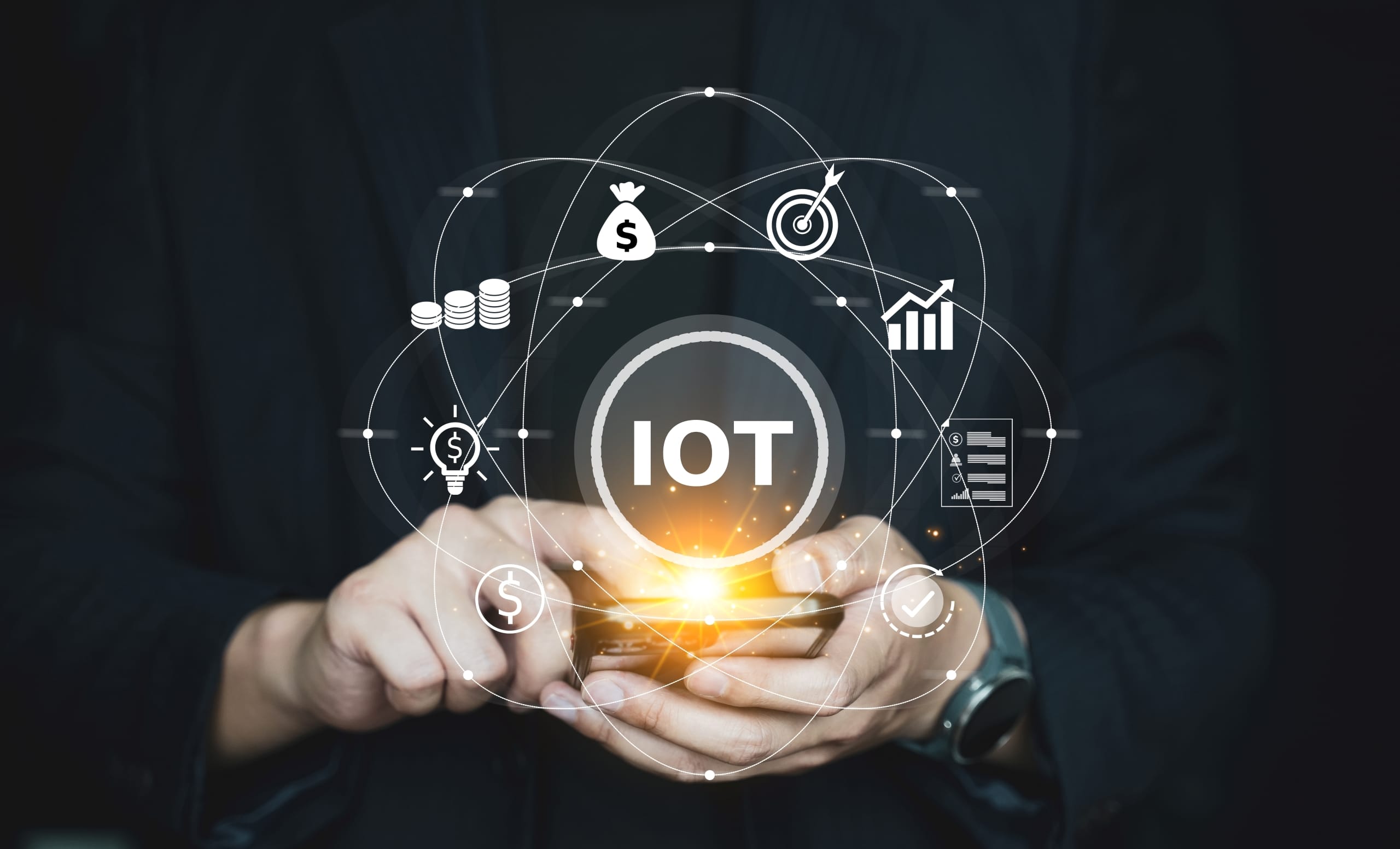 Hände halten ein Smartphone mit leuchtendem Display und darüber zentriert das Akronym IOT
